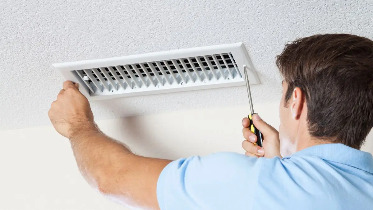 Technician cleans ceiling air duct with vacuum hose in modern home